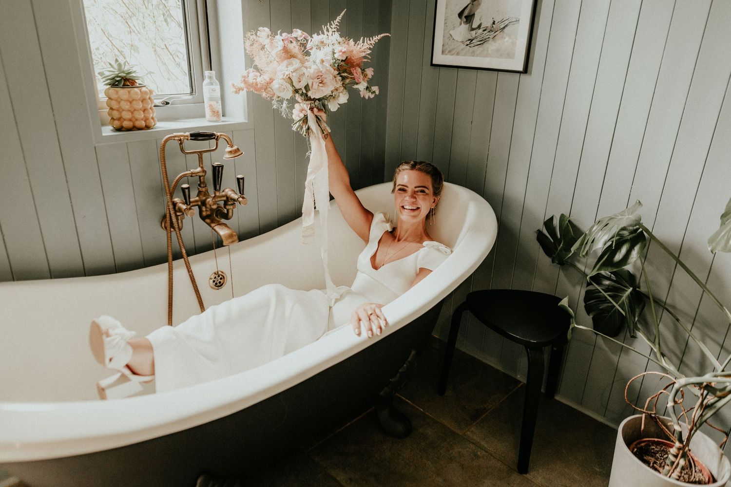 Woman relaxes in a luxurious clawfoot bathtub surrounded by white shiplap walls and orchid flowers.