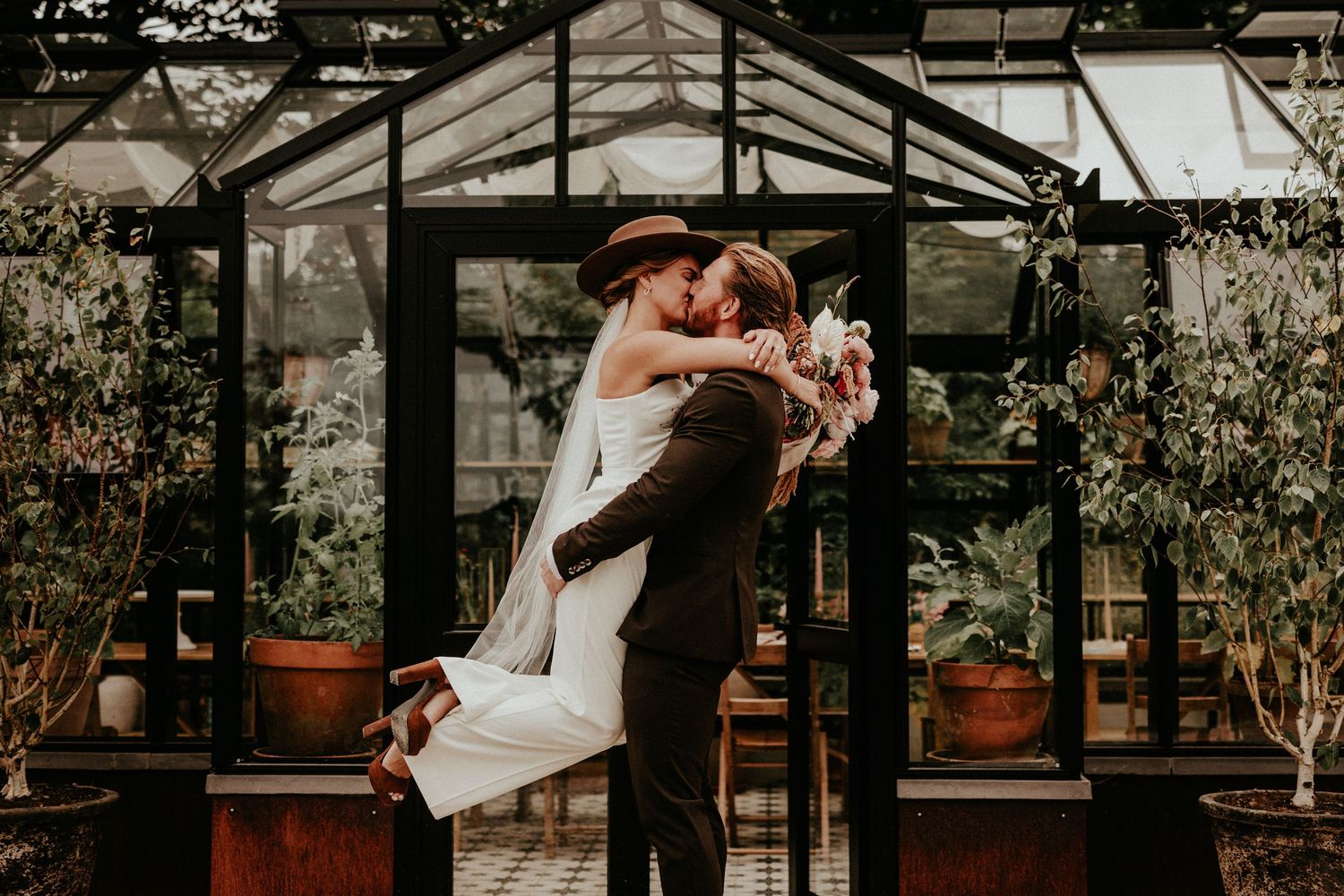 A couple shares a romantic moment during their wedding celebration in a rustic greenhouse setting.