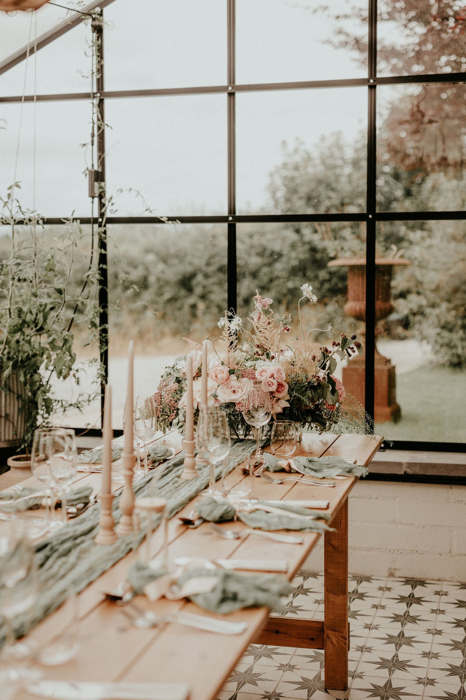 Elegant wedding reception table settings with soft pink floral arrangements in a sunlit greenhouse venue.