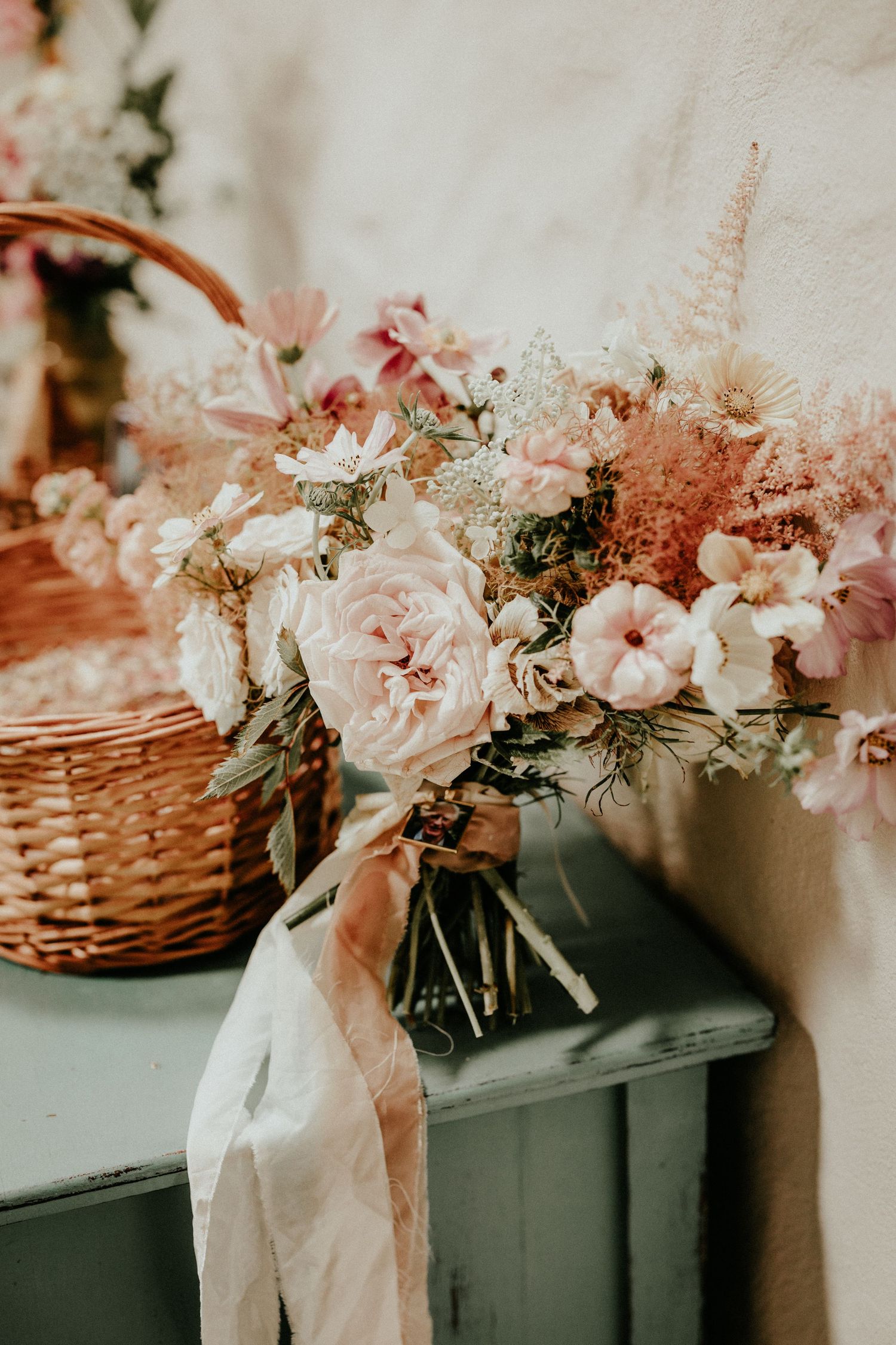 Delicate pink and white floral arrangement with roses in a vase tied with silk ribbon against a soft background.