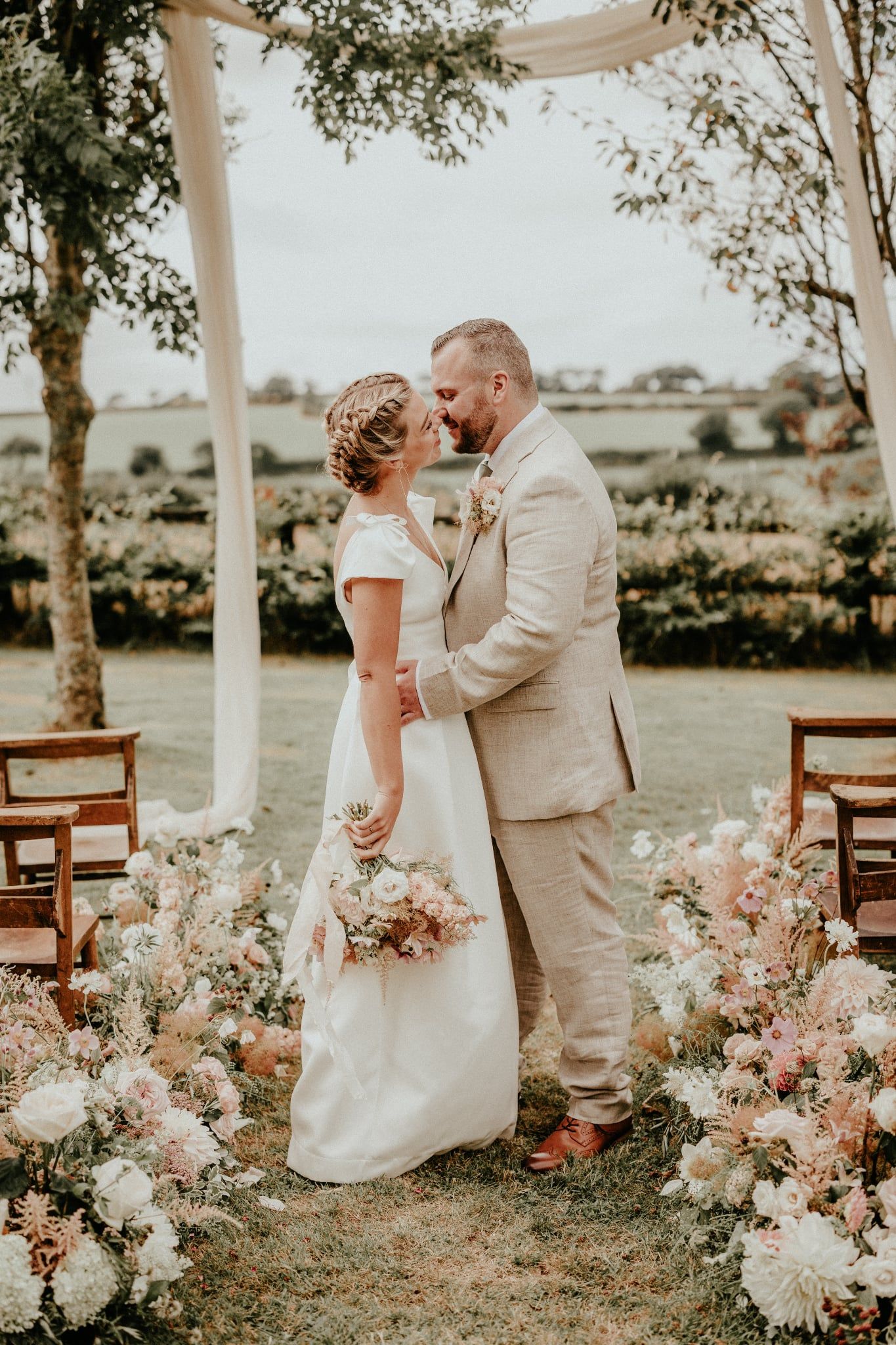 A tender wedding moment captured under a floral arch with soft lighting and romantic garden decorations.