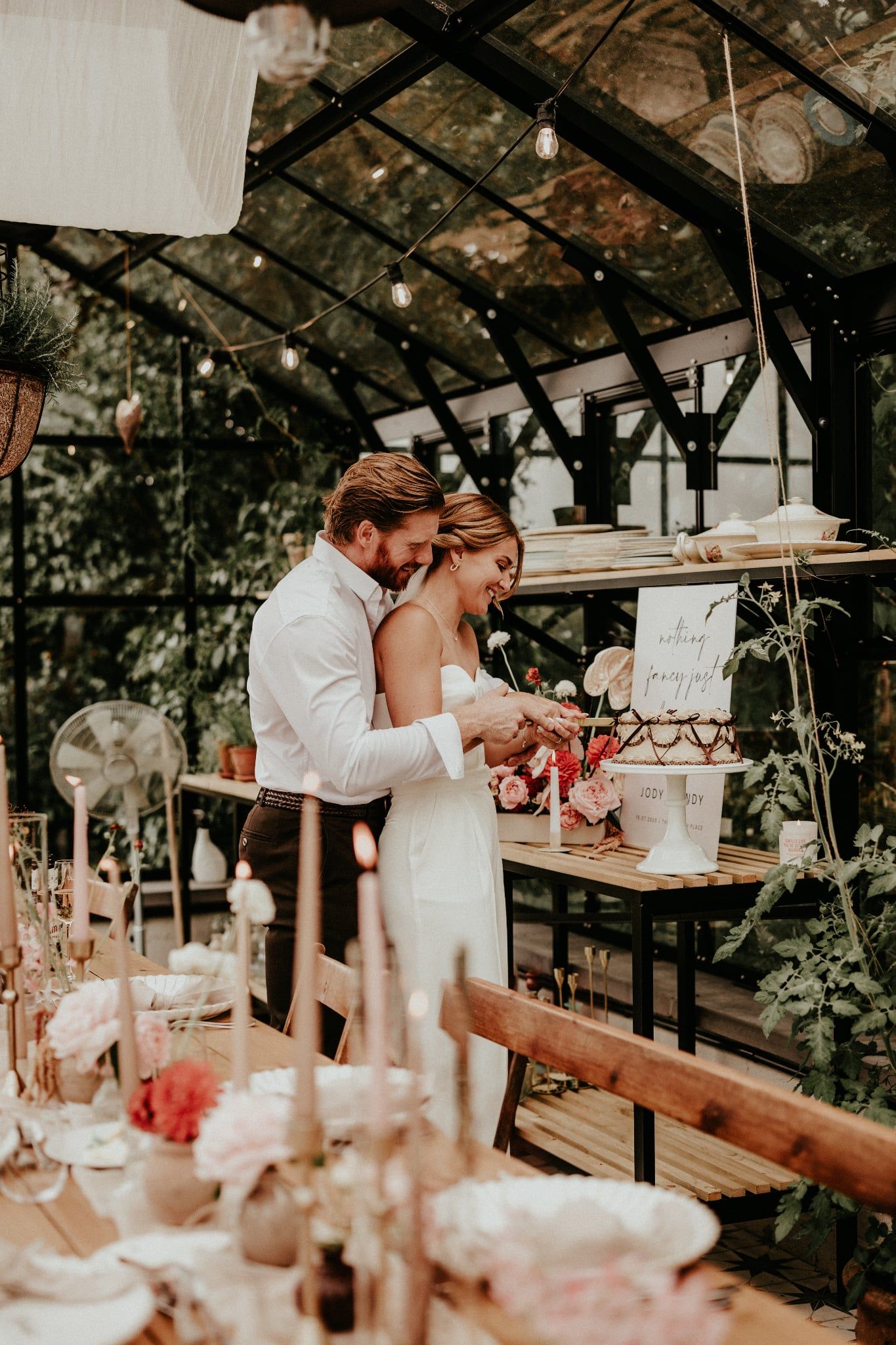 A couple shares an intimate moment at their wedding reception in a rustic greenhouse venue with soft lighting.