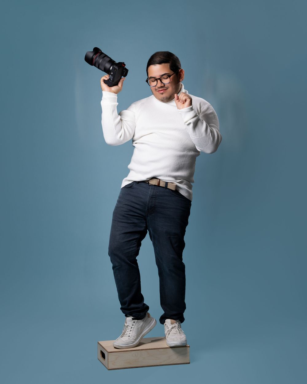 A person in a white sweater and dark pants demonstrates stepping up onto a cardboard box against a blue backdrop.