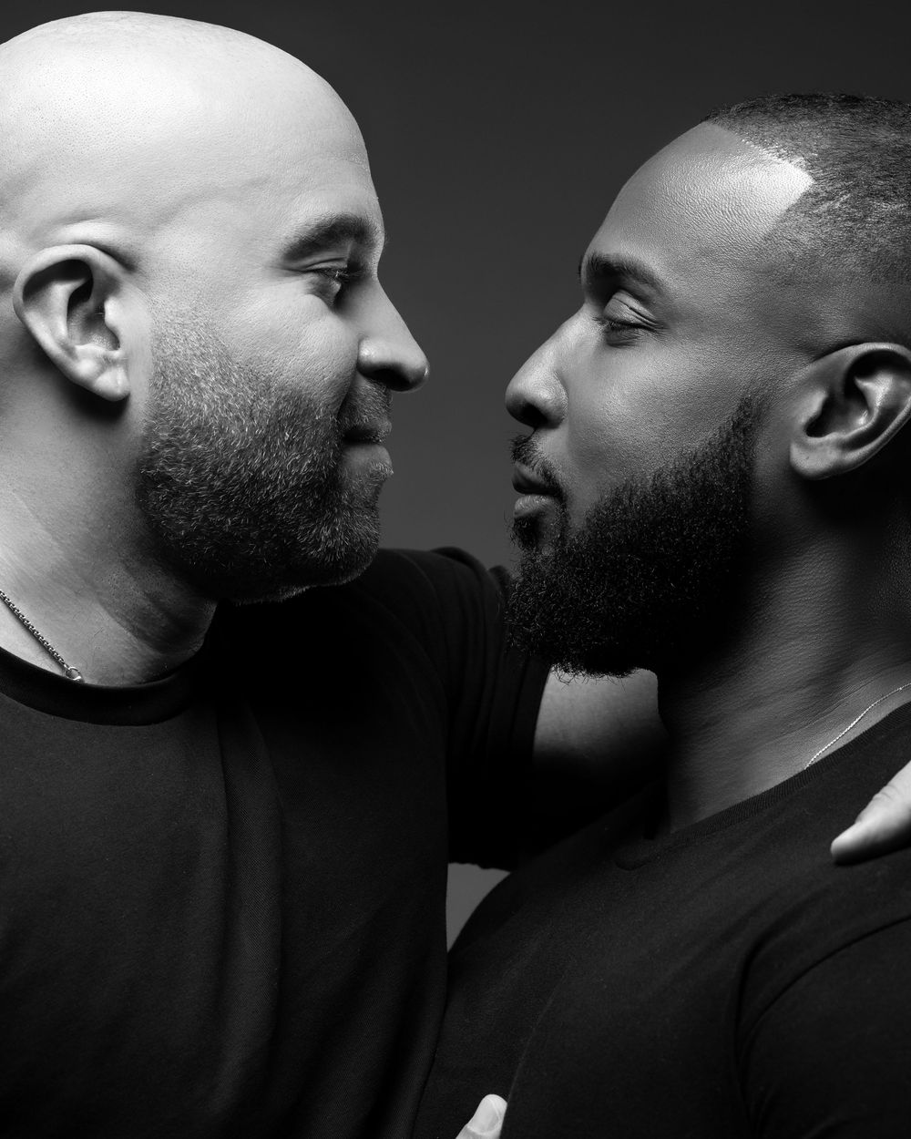 Black and white profile portraits showing two men in close proximity with dramatic lighting and dark backgrounds.