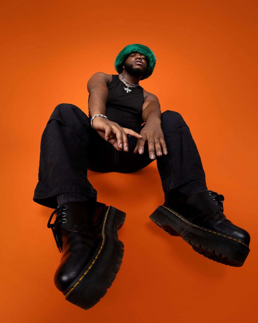 Artistic sequence of black boots and clothing against vibrant orange background creates dynamic visual movement.
