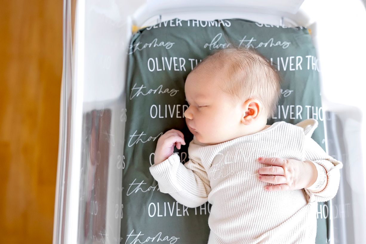 Baby lying on back against chalkboard background with handwritten text displaying names and measurements.
