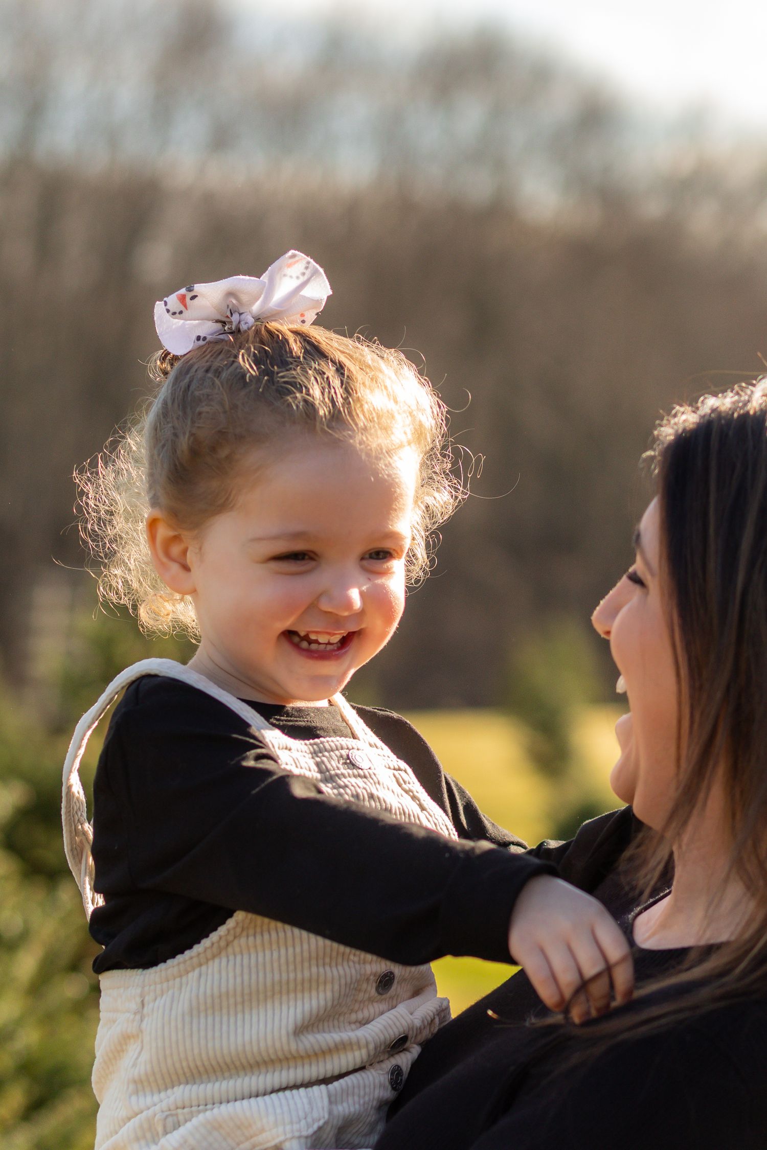 A tender moment captured at sunset as a child in a cream sweater playfully interacts with her mother in a black shirt.