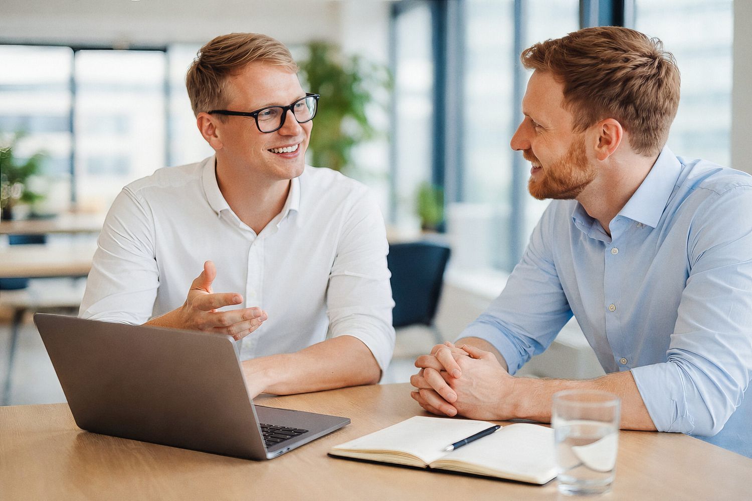 Two business professionals collaborate at a modern office desk with laptops and paperwork.