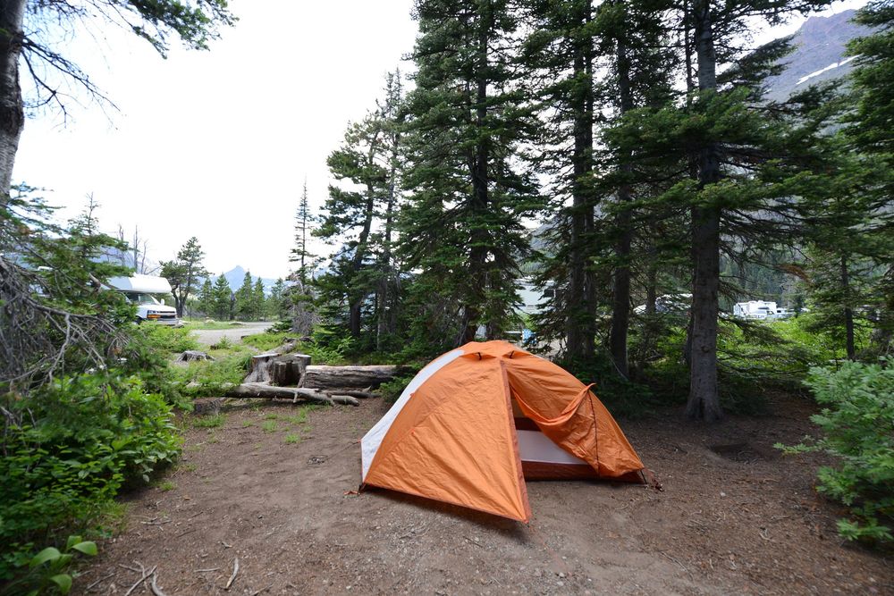 Orange camping tent set up at forested campsite with picnic table and mountain views in background.