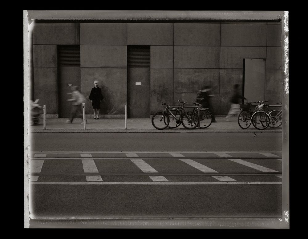 Black and white urban street scene with parked bicycles along concrete building wall.