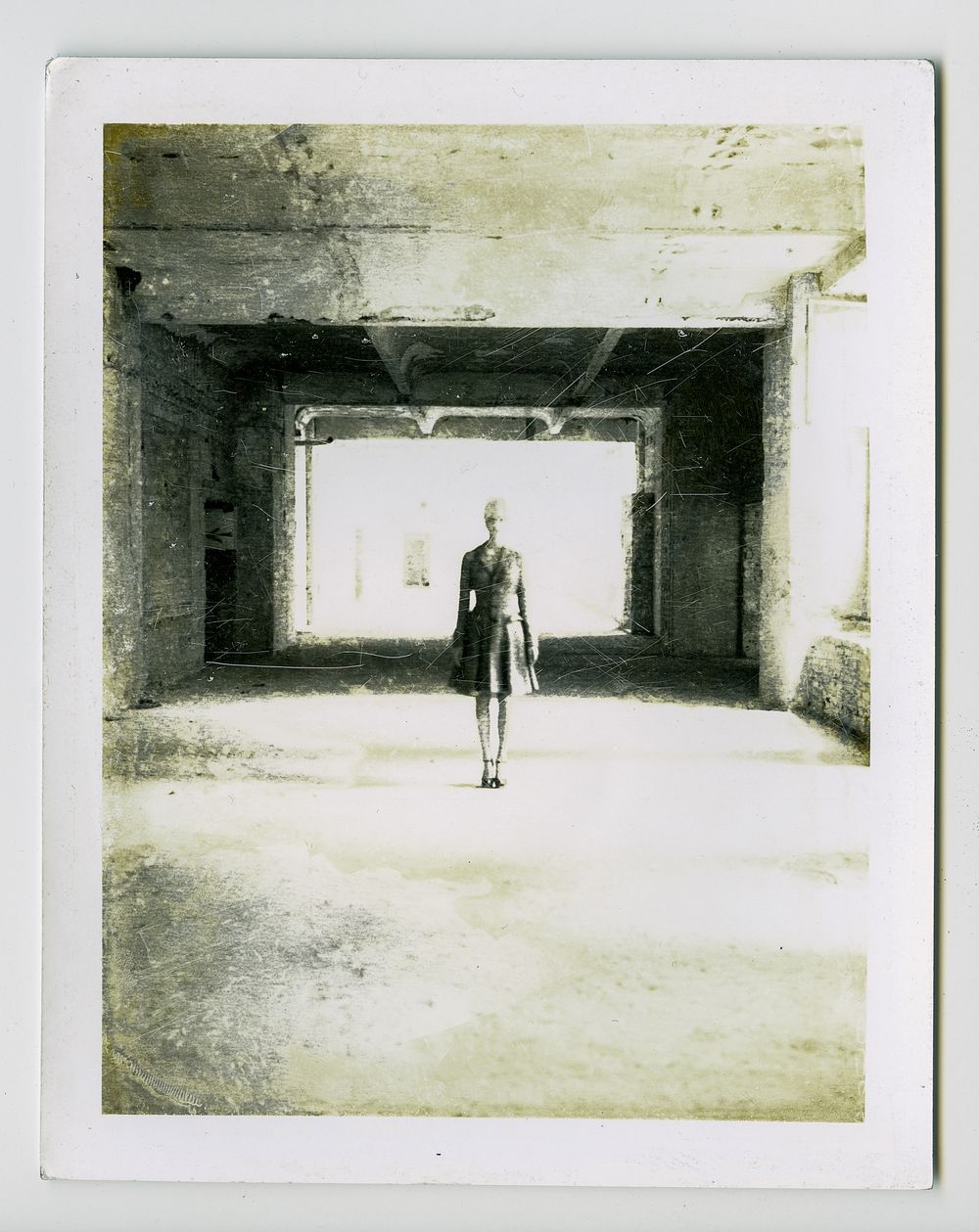 A silhouetted figure stands alone in a stark concrete tunnel with bright light pouring in from the far end.