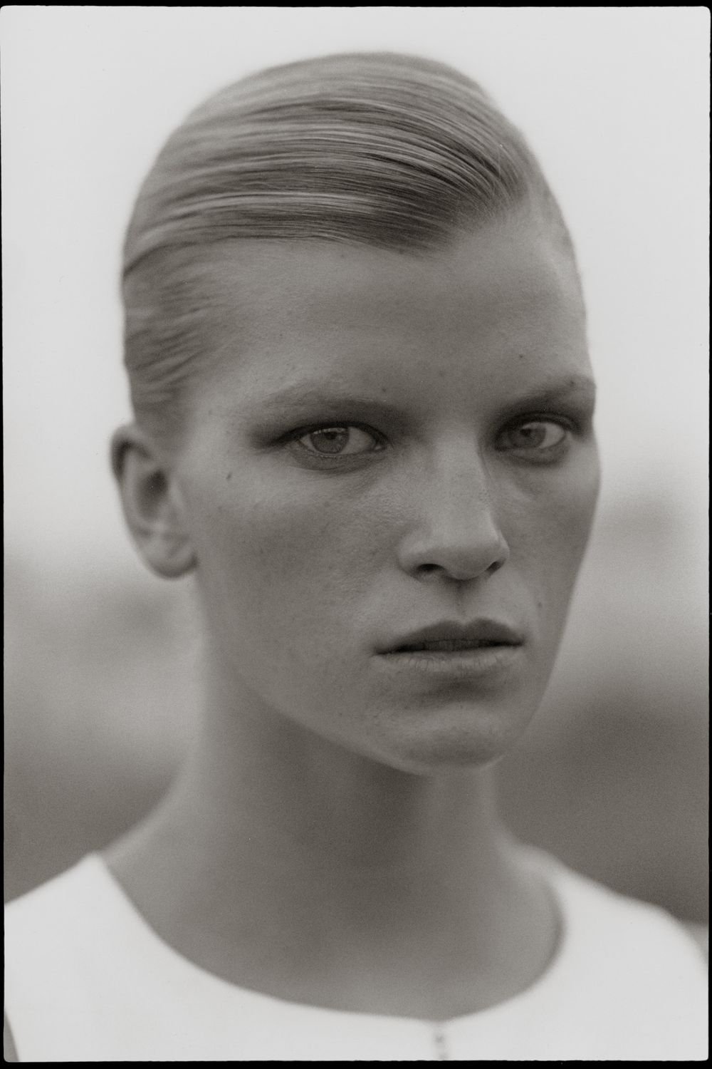 Black and white portrait photograph showing intense gaze and sleek pulled-back hairstyle against blurred background.