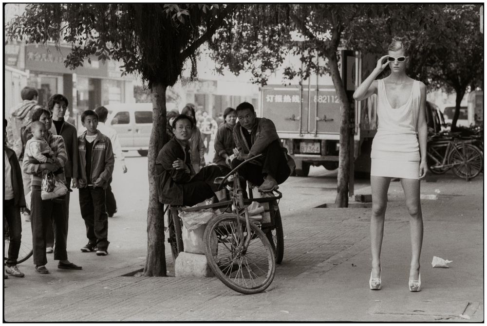 A black and white panoramic street scene shows people walking and bicycles along a city sidewalk in vintage attire.