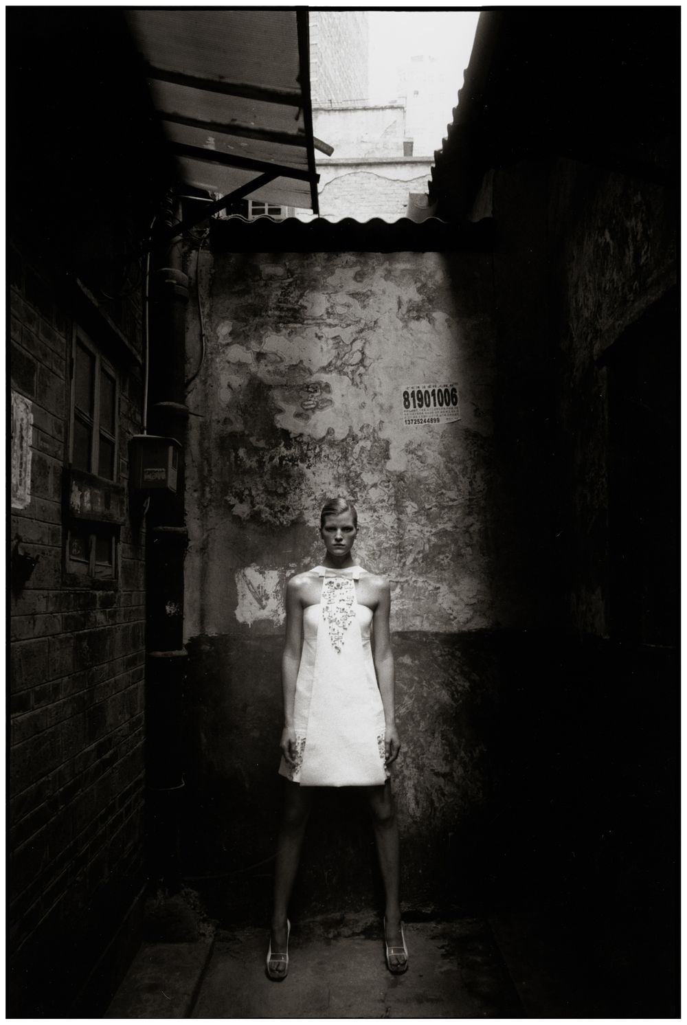 A haunting black and white photo series shows a figure standing against textured walls in a dark, moody setting.