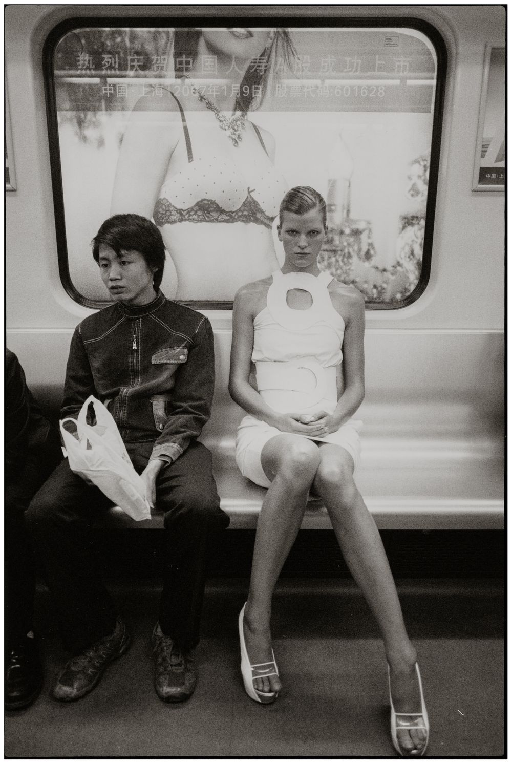 Two passengers sit apart on a subway train in a black and white candid photograph.