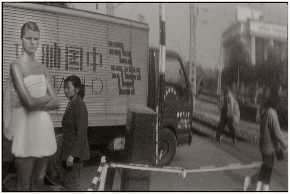 A vintage black and white street scene shows people gathered around a delivery truck in an urban setting.