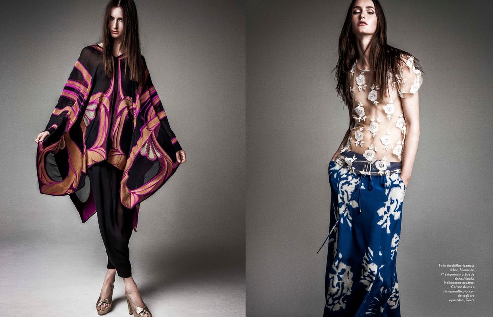 Fashion model wearing dramatic pink patterned poncho and model in floral print pants with white top in editorial photoshoot.