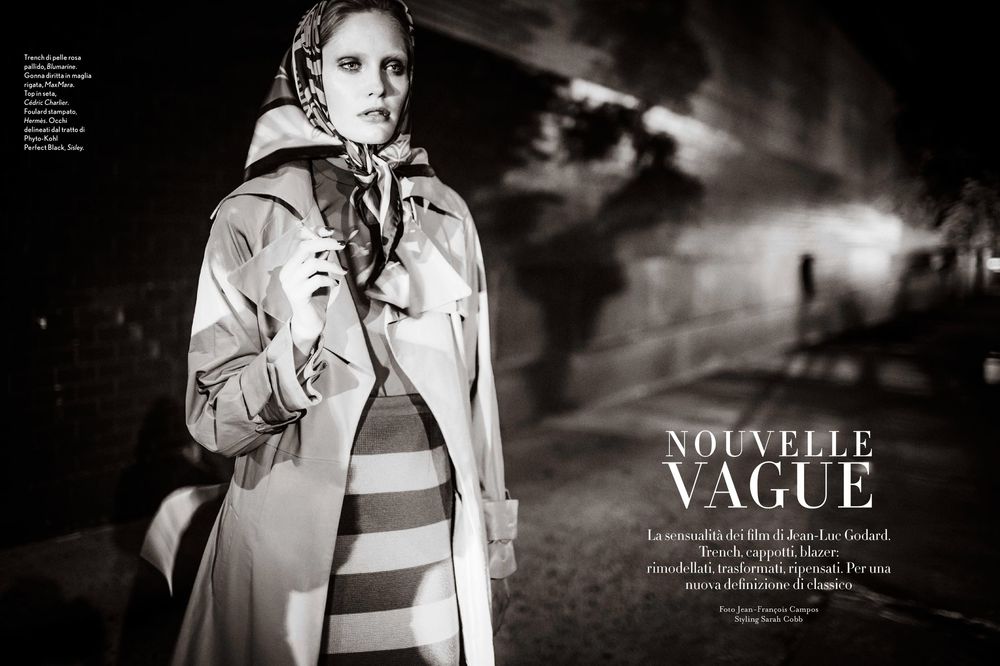 Black and white fashion editorial photo showing model in striped outfit and light trench coat against moody backdrop.