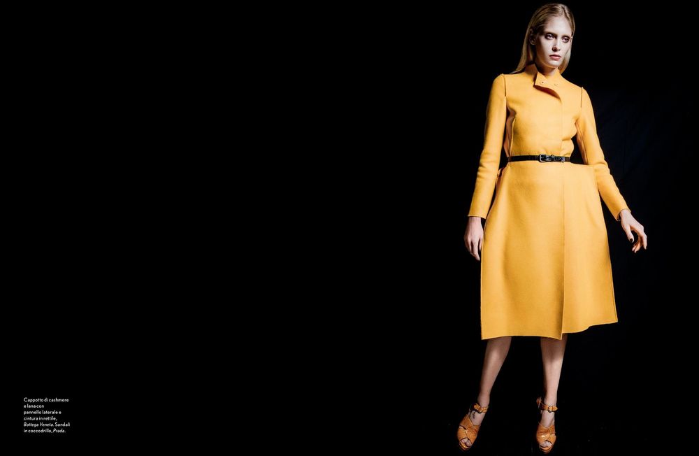 Fashion model wearing a mustard yellow belted dress with three-quarter length sleeves against dark background.