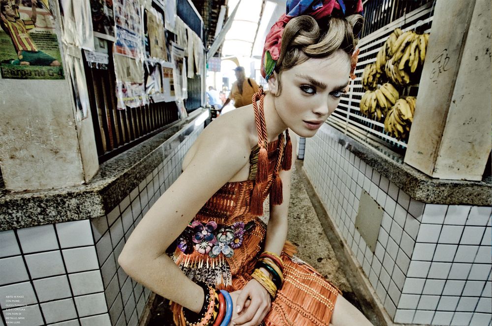Person in floral dress poses against tiled wall in artistic fashion photoshoot.