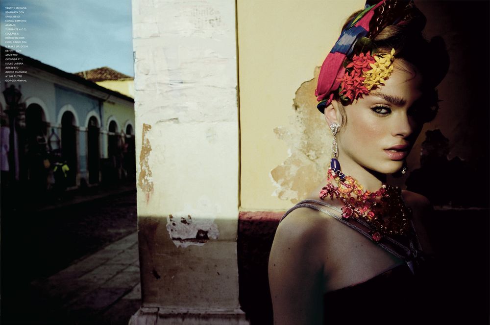 A fashion photograph showing vibrant tropical headpiece and jewelry against a backdrop of colonial architecture.