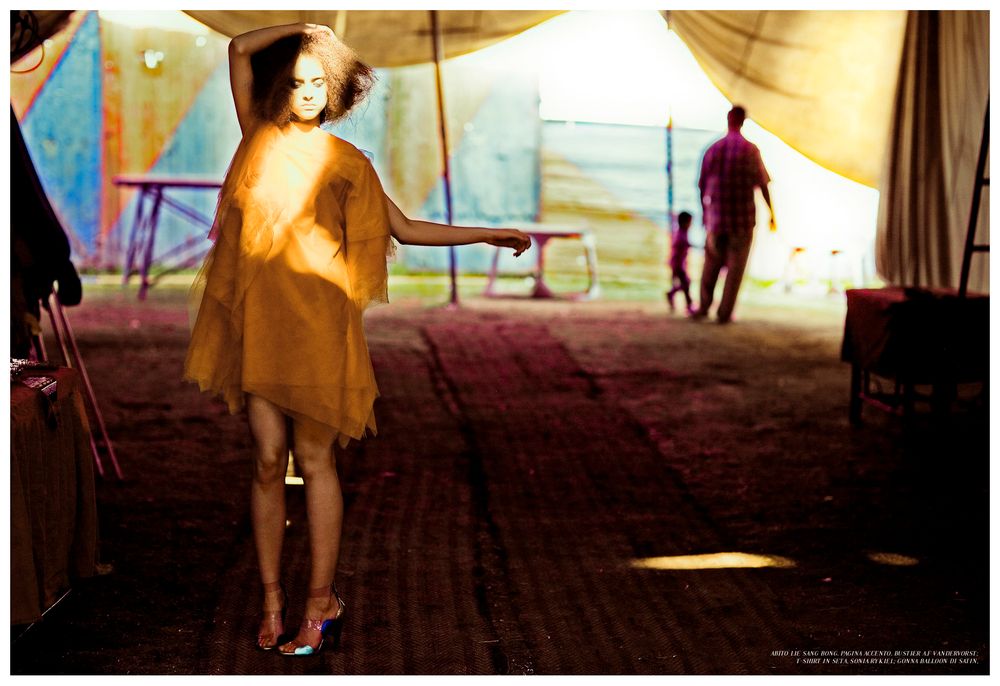 A silhouetted figure in a yellow dress walks through a sunlit indoor space creating dramatic shadows and light.