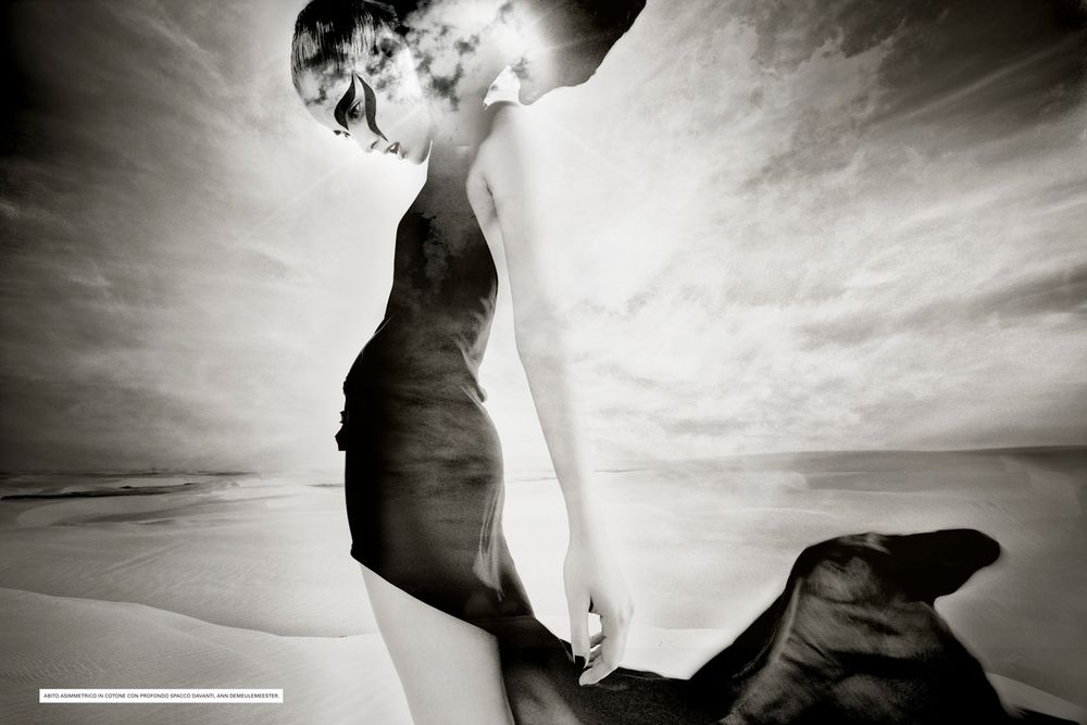 A dramatic black and white silhouette of a figure and flowing fabric against a cloudy sky at the beach.