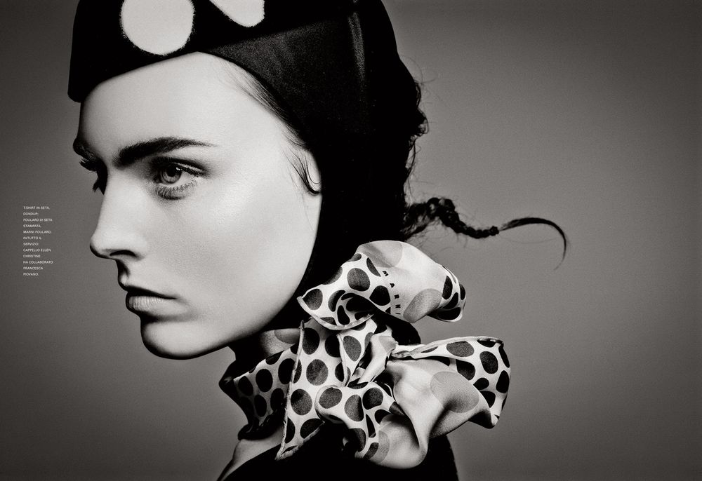 A dramatic black and white fashion portrait showing a side profile with a giraffe-print scarf against dark background.