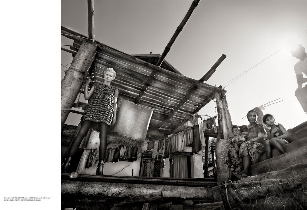 Black and white photograph showing a rustic shack with laundry hanging and makeshift metal roofing.