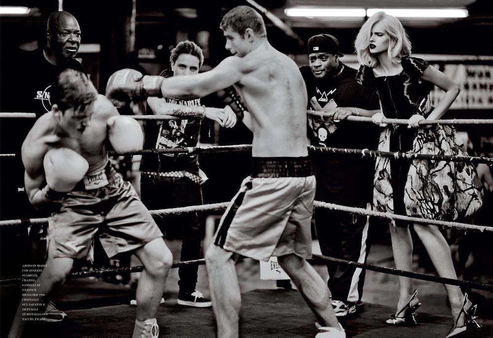 Two boxers spar in a boxing ring while a spectator watches from ringside.