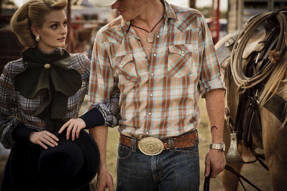 Western-styled figures stand together near horse tack, featuring plaid shirt and decorative belt buckle details.