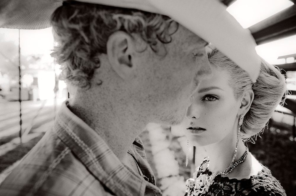 A black and white artistic photograph showing two people in close proximity with one wearing a white hat.