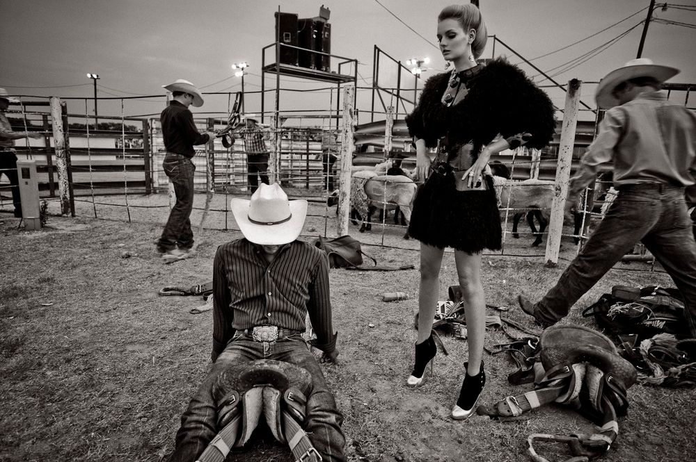 Black and white photo of a rodeo scene with a person in a cowboy hat seated on a bull while others stand nearby.