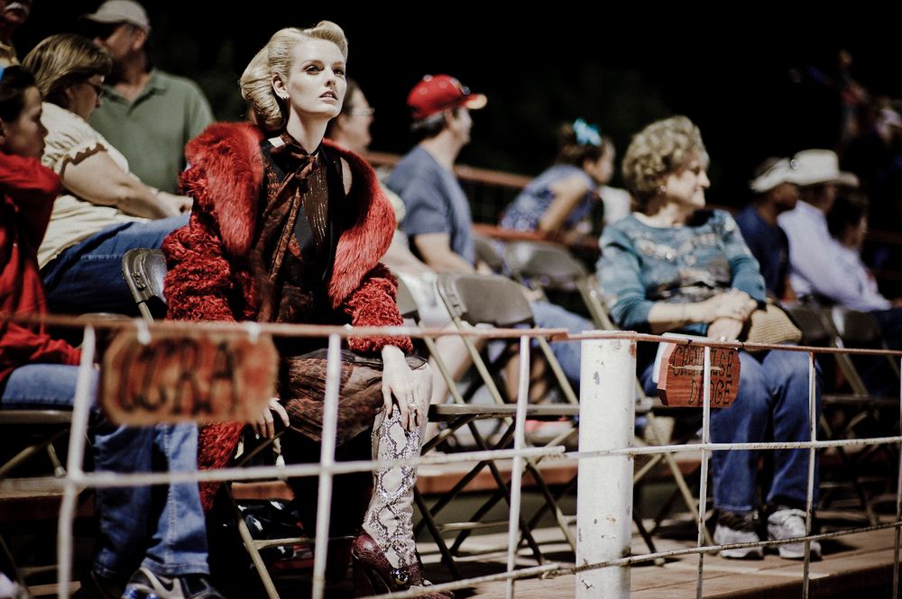 Spectators lean against a white railing while watching an event at an outdoor venue.