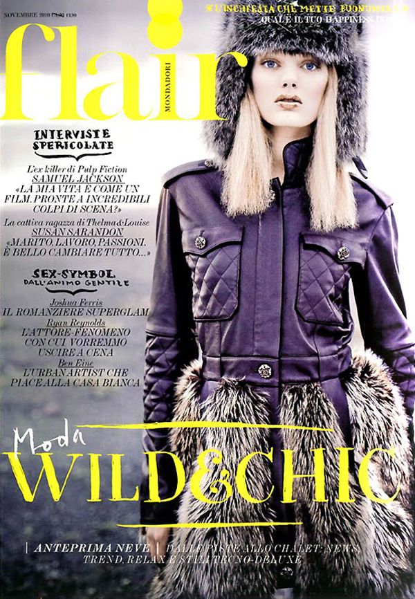 Fashion magazine cover featuring model in purple coat with fur trim against dark dramatic backdrop.