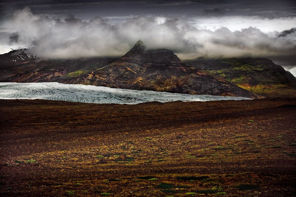 Dramatic aerial panorama of rugged mountain landscapes with dark clouds and misty atmosphere over barren terrain.