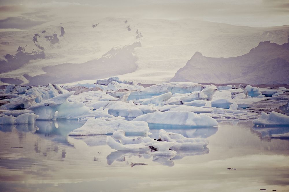 Aerial view of a vast icy landscape with snow-covered terrain stretching to the horizon under pale skies.