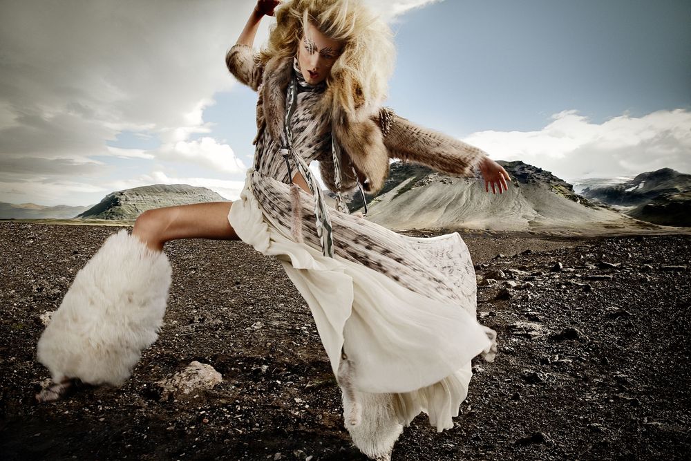 A flowing white dress billows dramatically against a rocky mountain landscape under moody clouds.