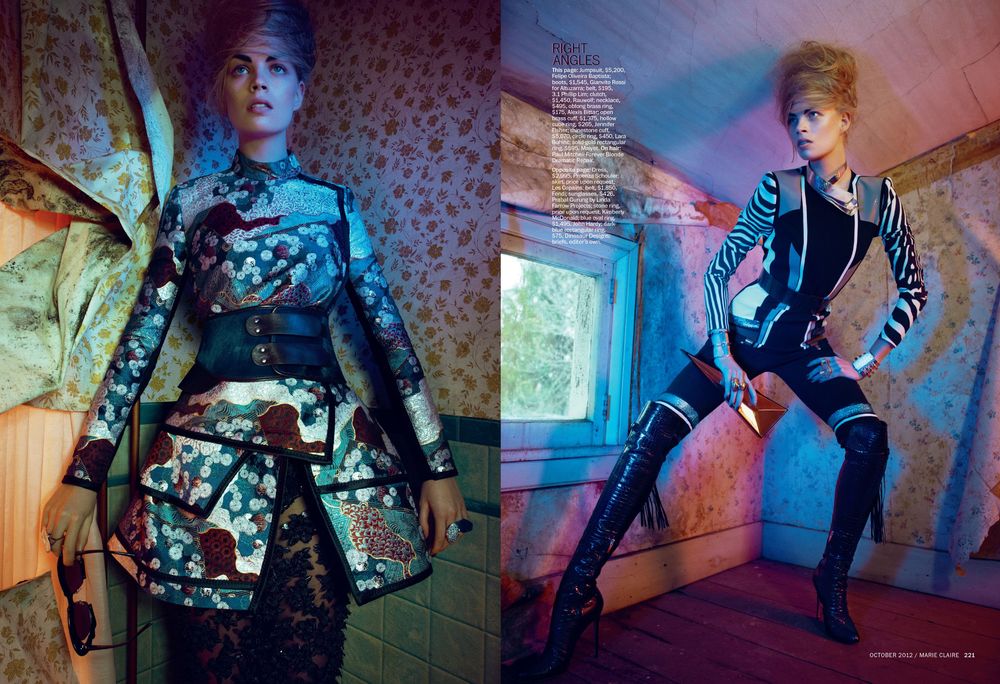 Fashion model poses in avant-garde outfit against colorful neon lighting and patterned wallpaper in artistic photoshoot.