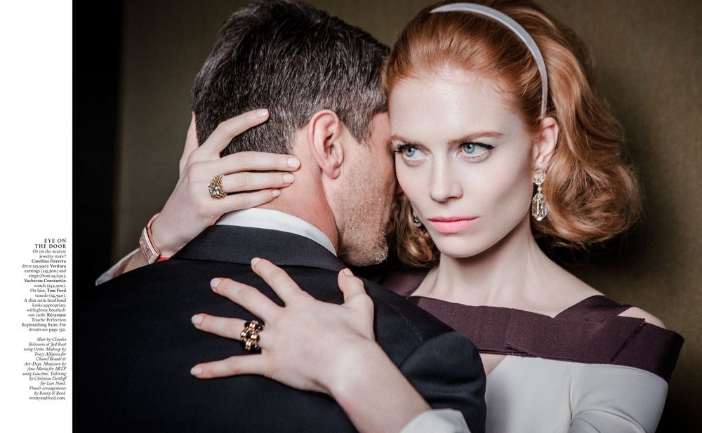 A dramatic black and white fashion photograph showing an intimate embrace between two figures in formal attire.