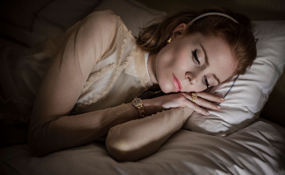 Person sleeping peacefully in white bedding with soft natural lighting casting shadows across the scene.
