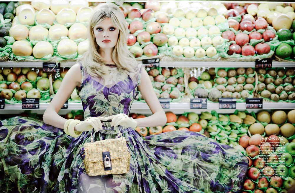 Fashion editorial photoshoot in a grocery store produce section with purple floral dress among fresh fruits.