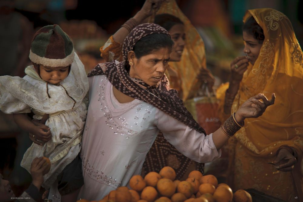 A vendor arranges fresh oranges at a bustling market stall in India.