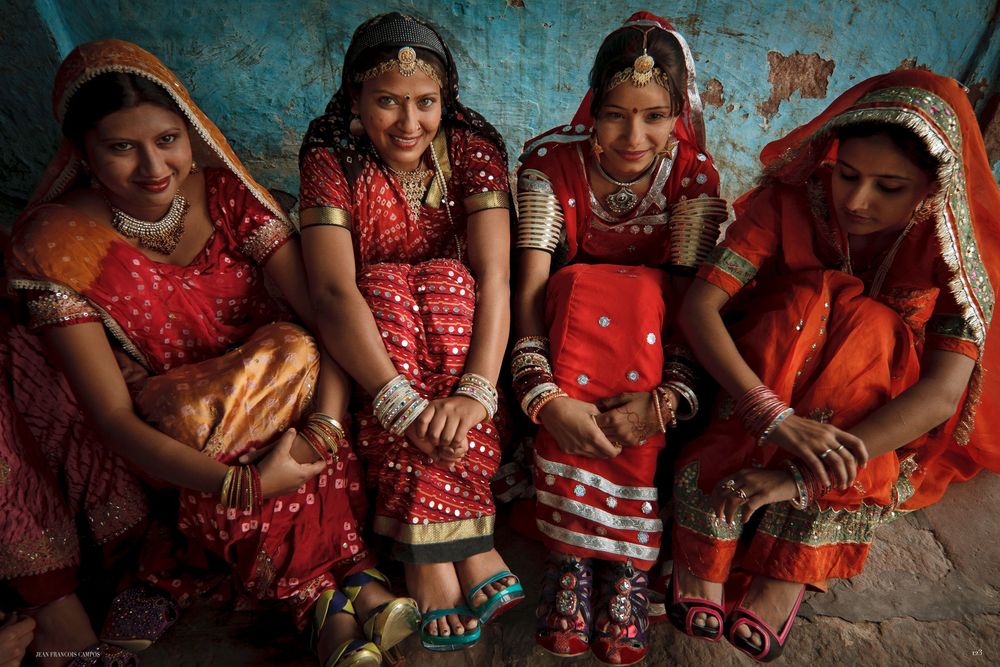 A group of women wearing traditional red and gold Indian saris sit together during a cultural celebration.