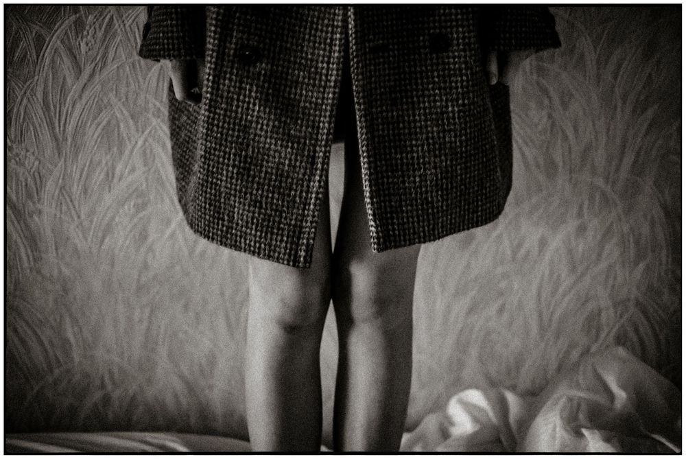 Black and white photograph showing a person wearing a tweed skirt standing against a textured background.