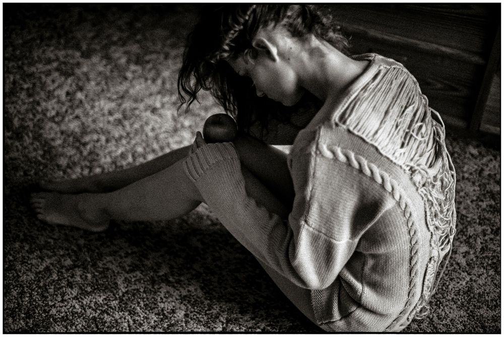 Black and white photograph of a person lying on carpet with head tilted back in an emotional pose.