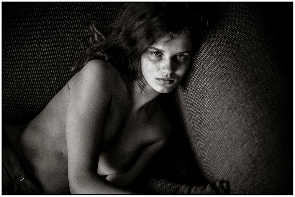 Black and white portrait photograph of a woman lying down on a textured surface, looking at the camera.