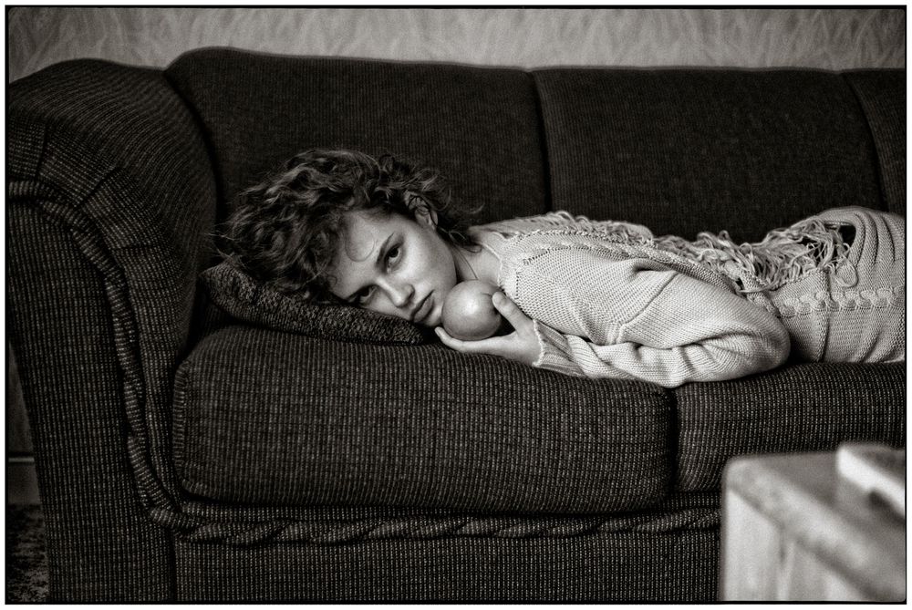 Black and white photograph of a young child sleeping peacefully on a textured couch in soft lighting.