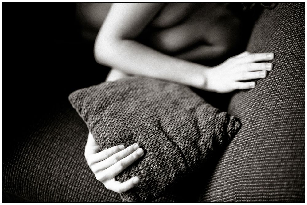 Black and white photo of a person hugging a textured pillow on a couch, conveying comfort and solitude.