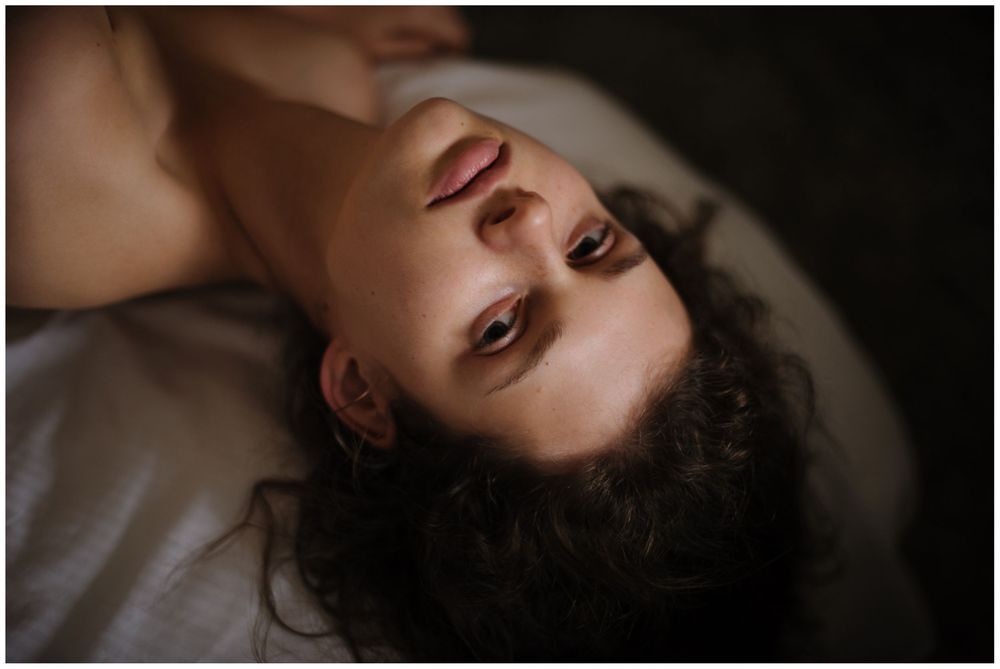A woman with curly hair lies back looking upward in a moody, artistic portrait shot from above.